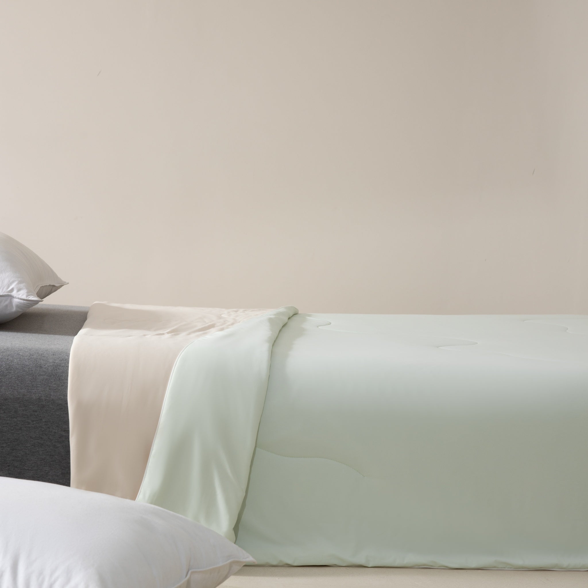 Close-up of a bed with light green bedding and pillows against a plain wall.