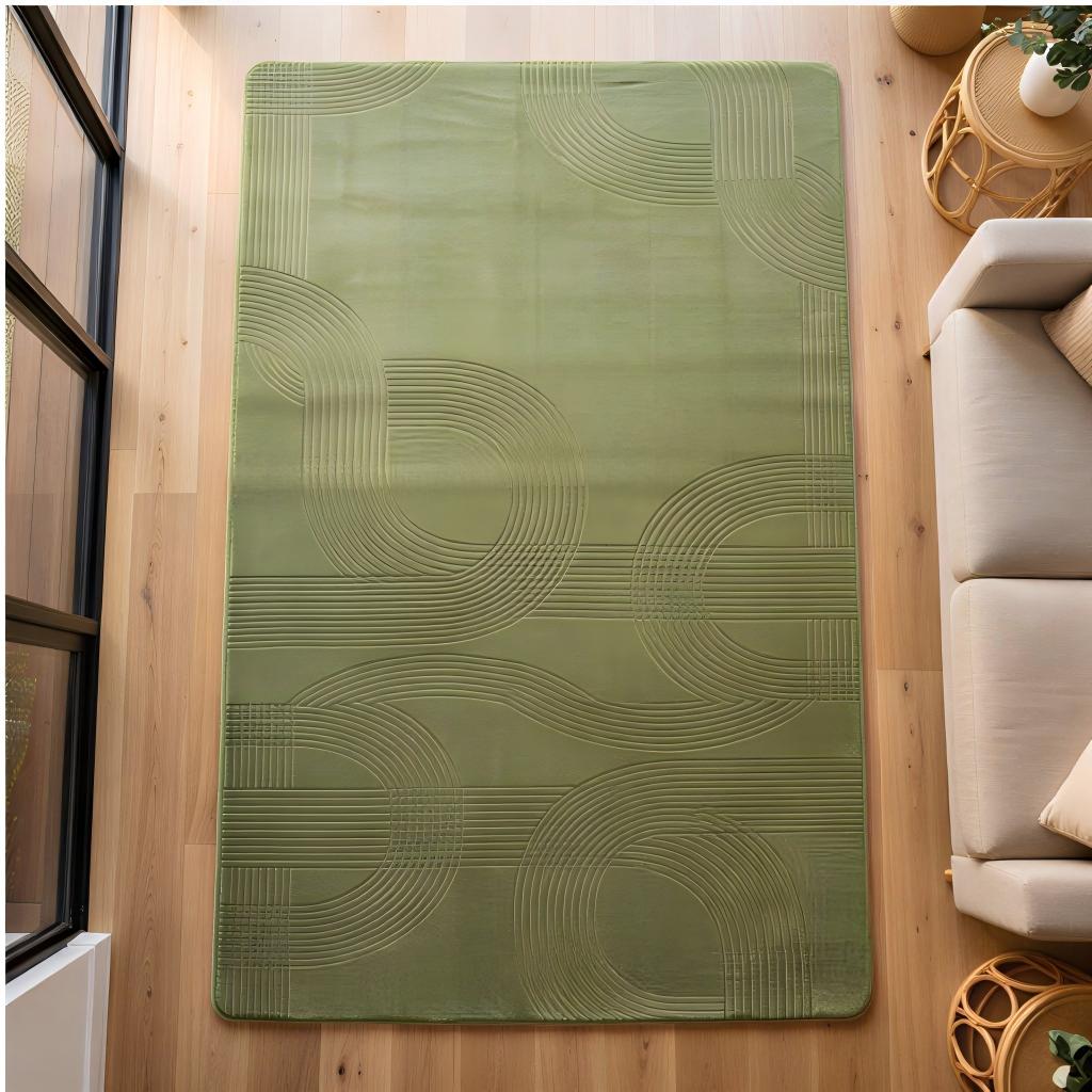 A rectangular sage green area rug with a raised wavy geometric pattern, displayed on a light wood floor in a modern living room setting next to a beige sofa.
