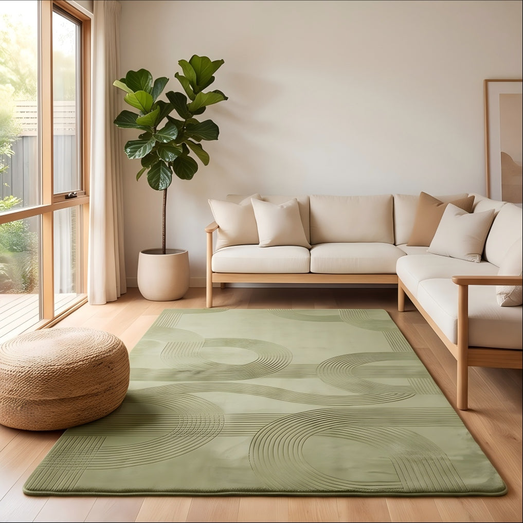 A sage green area rug with a wavy, abstract embossed pattern is styled in a bright, modern living room with a light wood sofa, beige cushions, a potted fiddle-leaf fig, and a woven pouf.