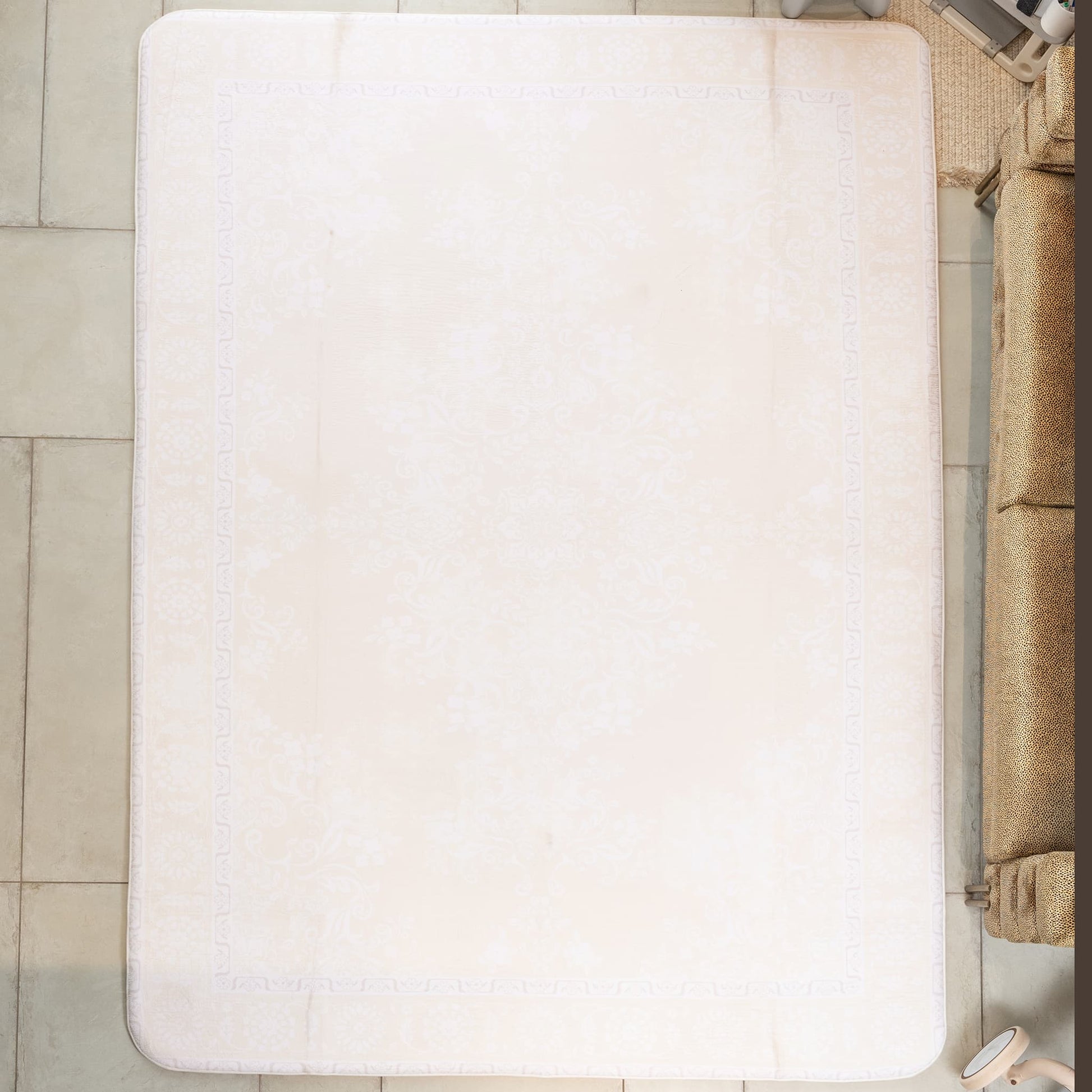 White bath mat on a tiled floor next to a brown sofa.