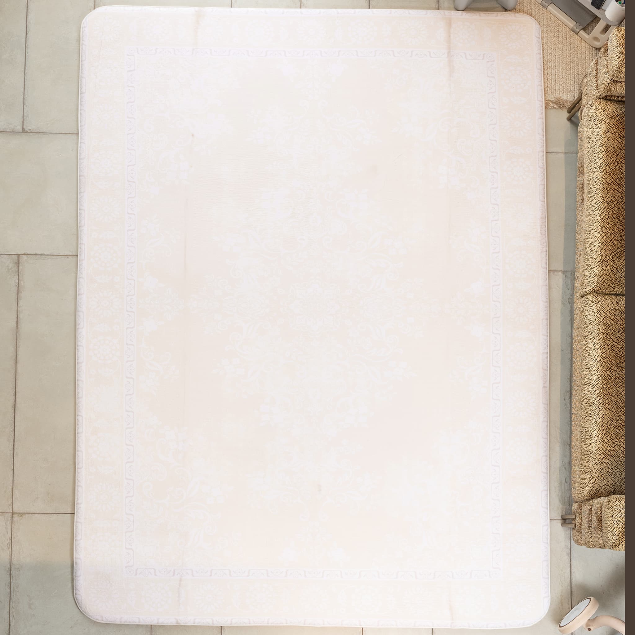 White bath mat on a tiled floor next to a brown sofa.
