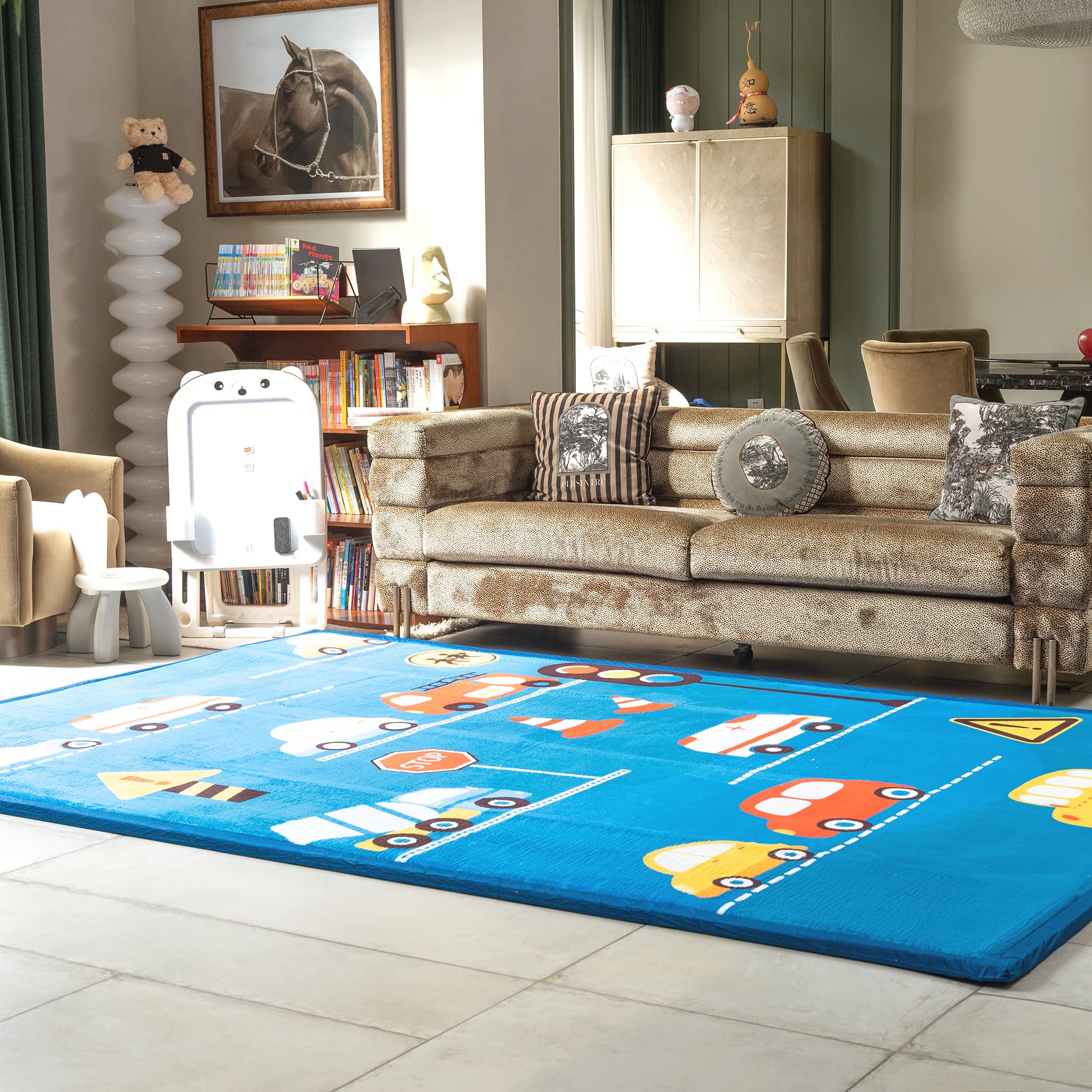 Children's room with a blue LuxKing Cloud rug featuring colorful car designs, a beige sofa, and toys.