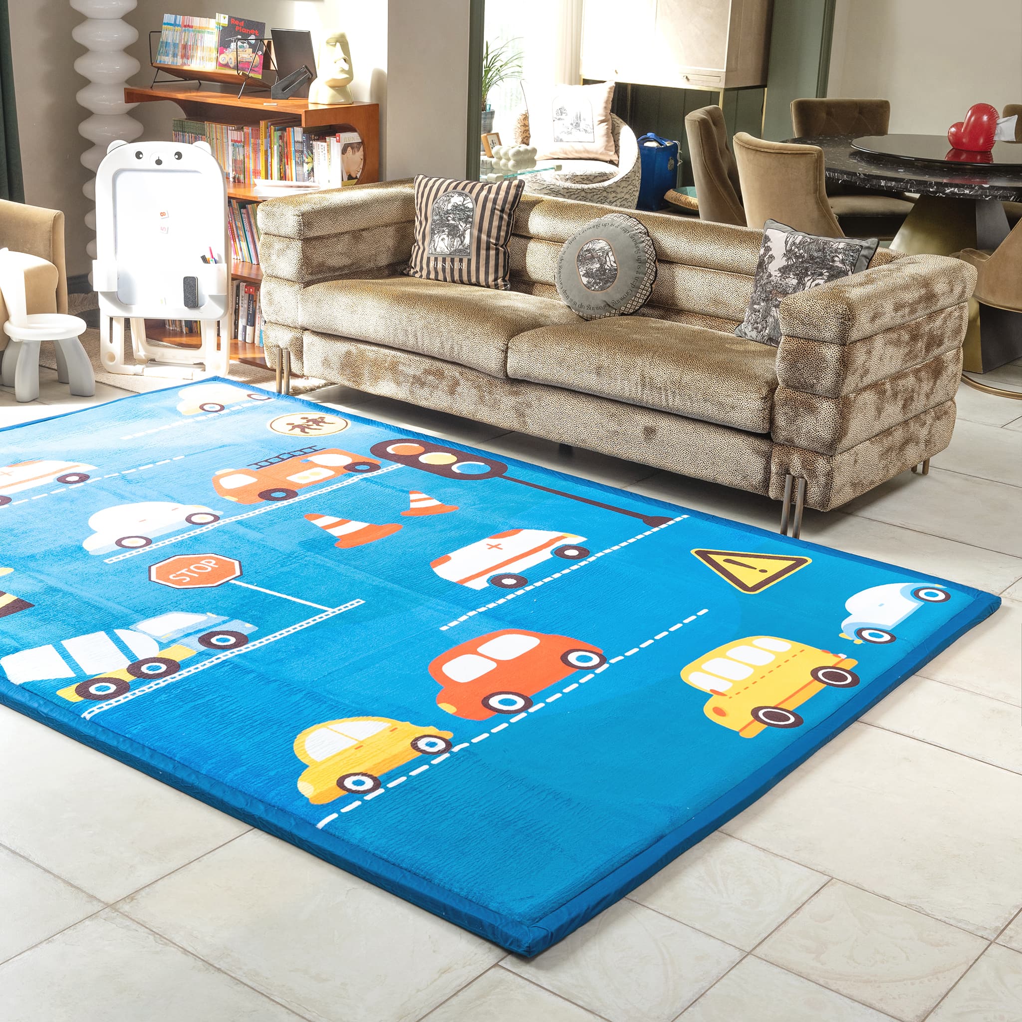 Children's playroom with a blue LuxKing Cloud Mat featuring colorful cars and traffic signs, a beige sofa, and a bookshelf