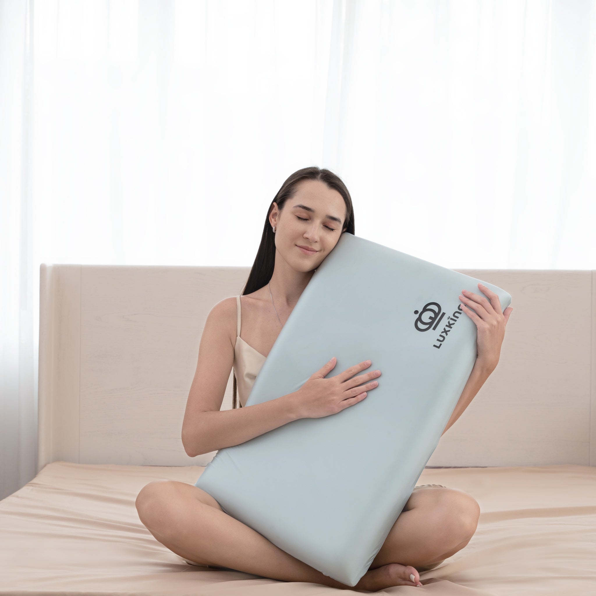 Woman holding a light blue pillow with a visible brand logo on a bed.