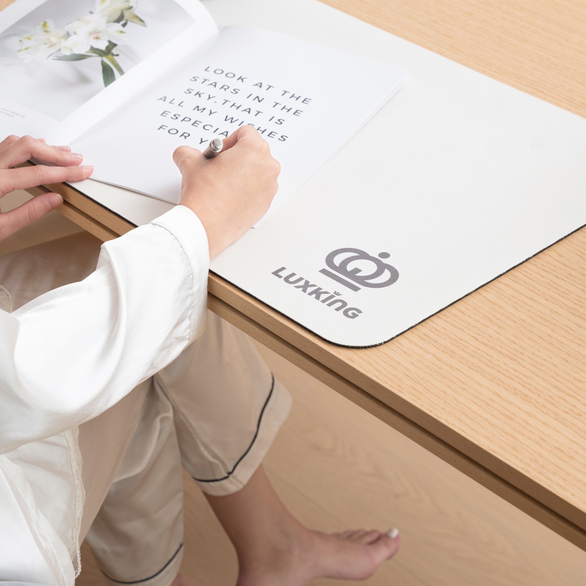 Person writing on a book with a pen, sitting on a wooden floor with a Luxking branded mat.