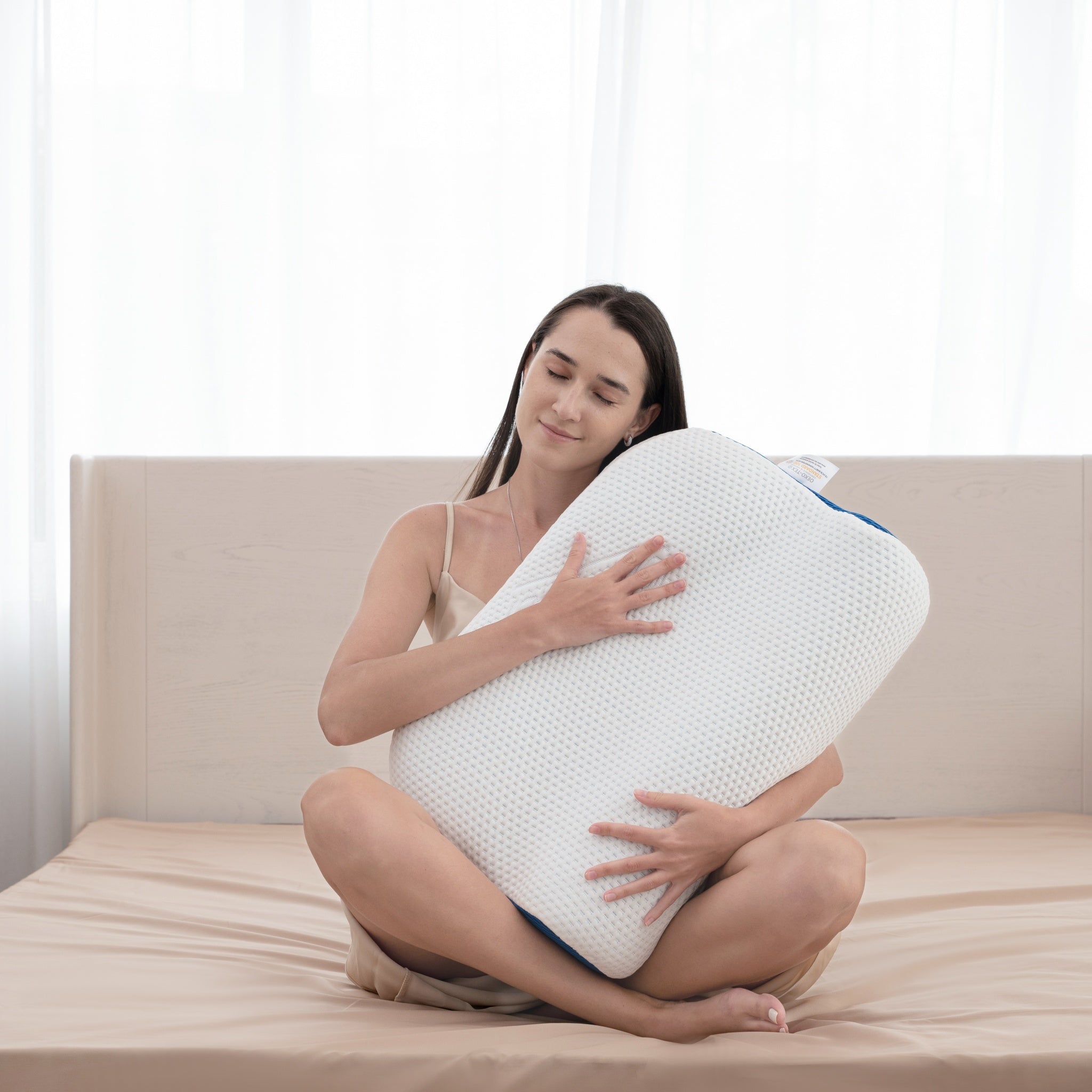 Woman holding a large white pillow on a bed