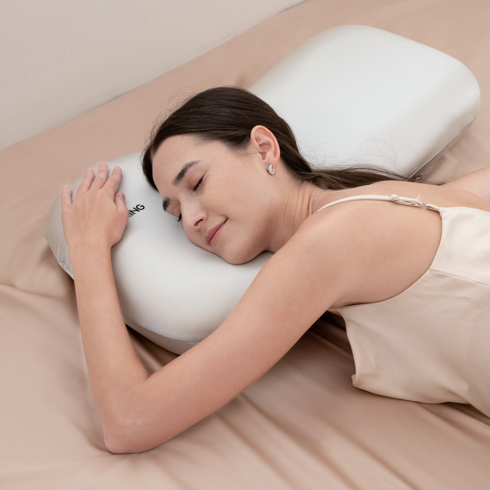 Woman sleeping on a white U-shaped pillow on a beige bed