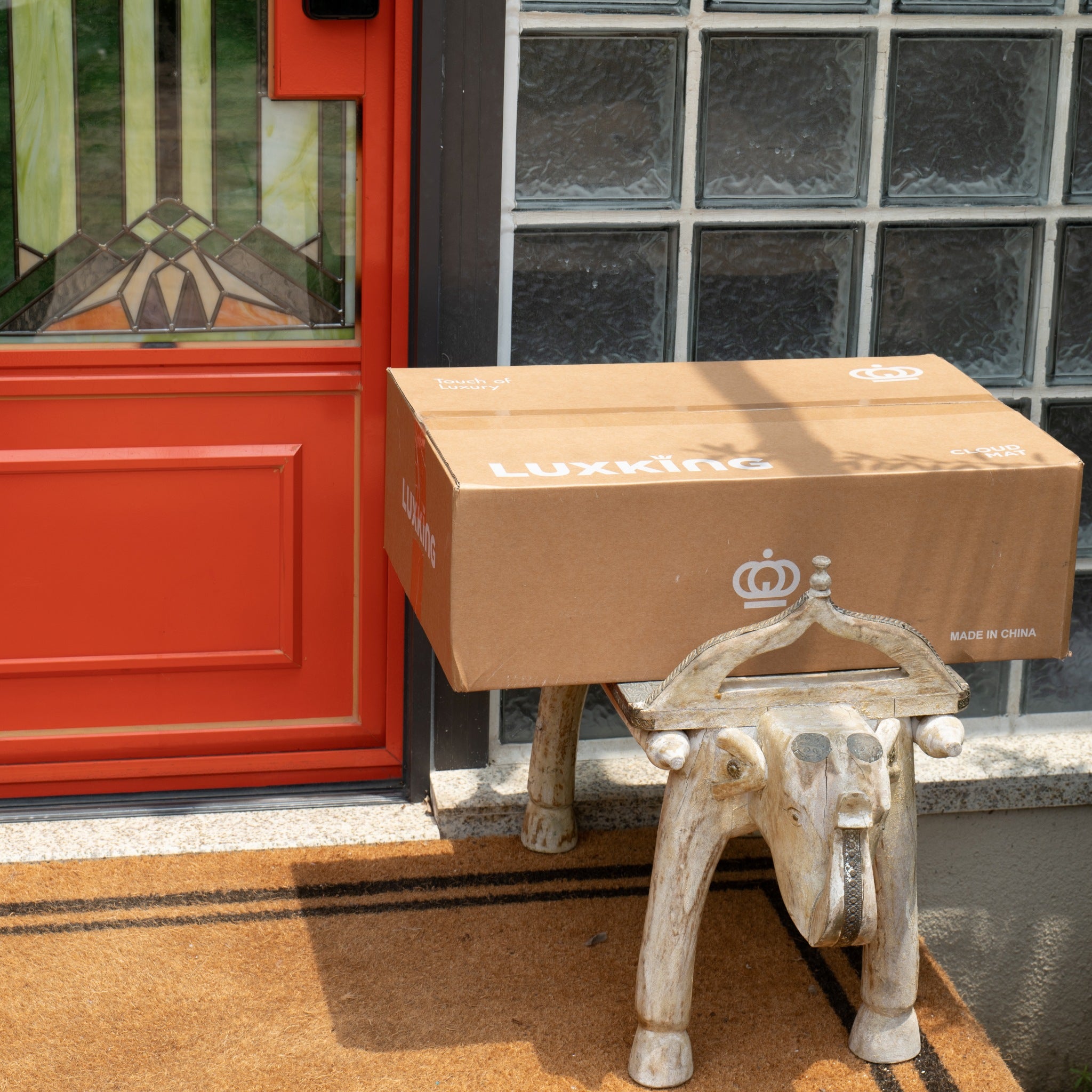 Cardboard box with 'Luxking' branding on a small wooden stool outside a building with a red door.