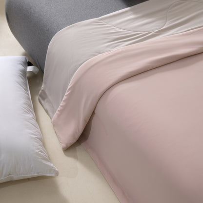 Close-up of a pink comforter and gray pillow on a bed.