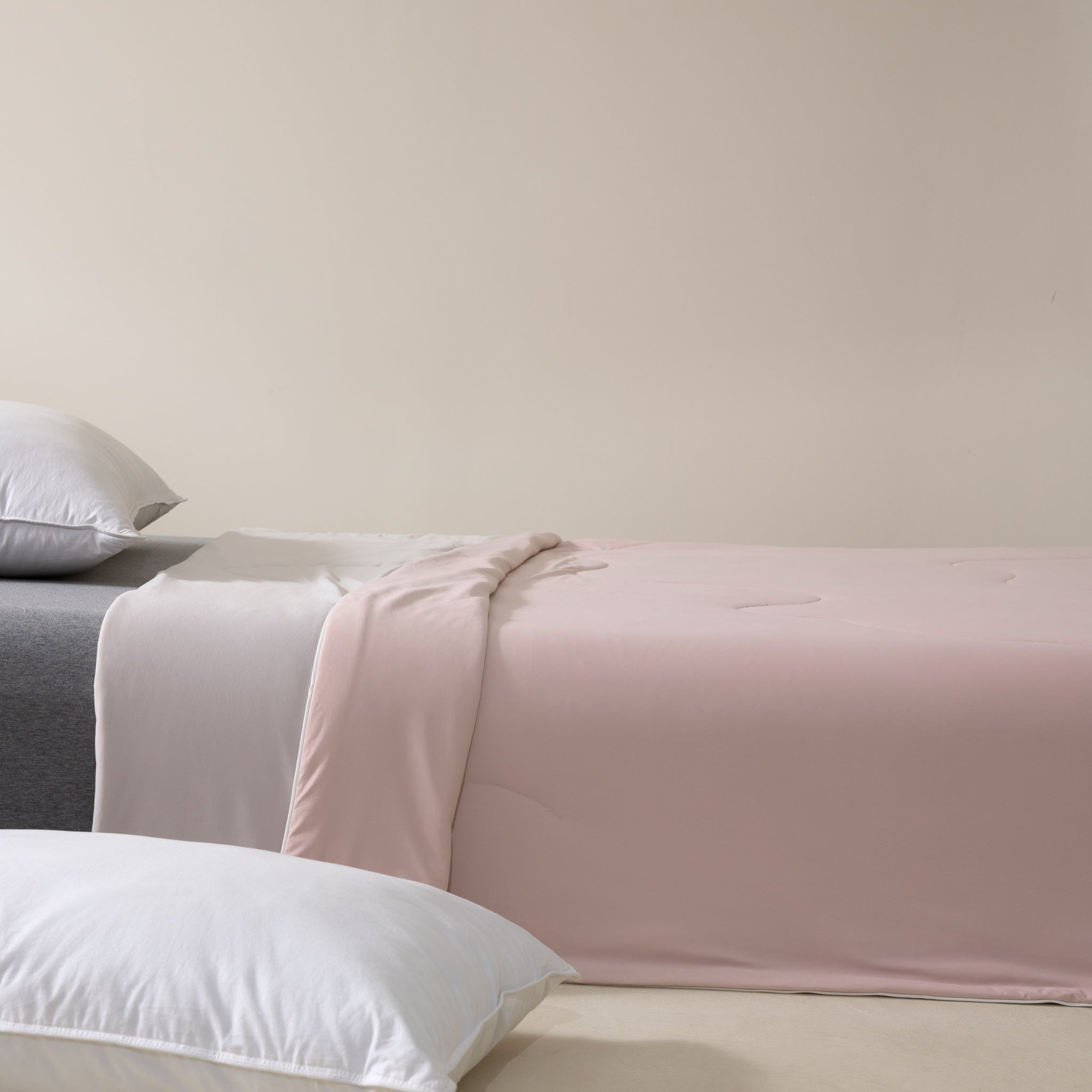 Bed with pink blanket and white pillows against a beige wall