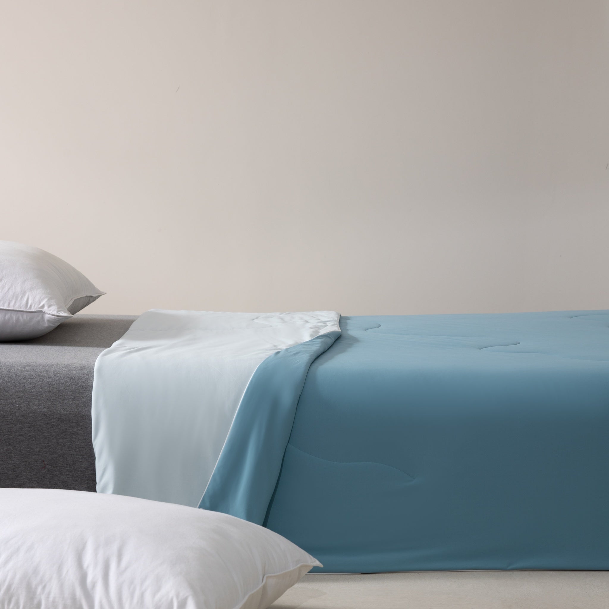Bed with blue bedding and gray mattress against a beige wall