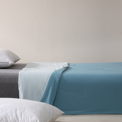 Bed with blue bedding and gray mattress against a beige wall
