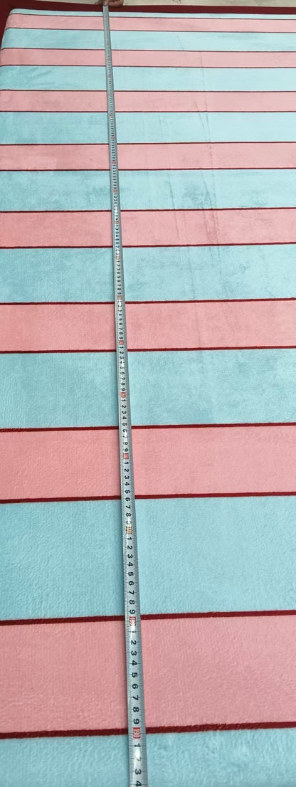 A striped textile, likely a blanket or towel, with alternating light blue and dusty pink horizontal stripes, shown with a metal measuring tape running vertically down the center.