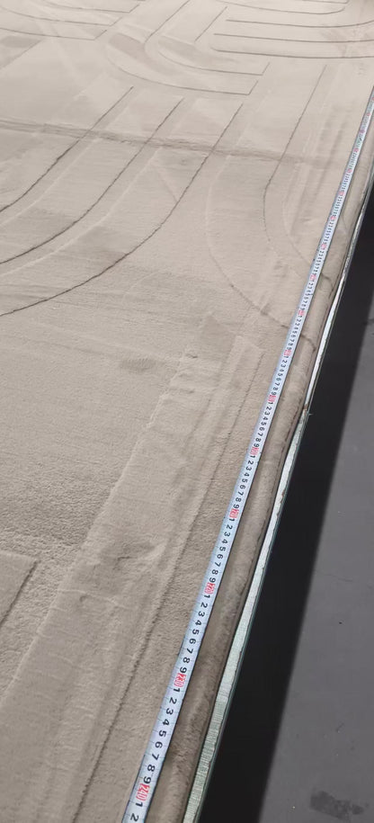A close-up view of a light beige textured carpet or rug with a white measuring tape laid along one edge to show the length.