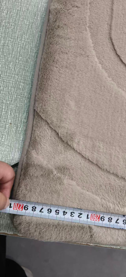 A close-up of a beige plush or fleece fabric product being measured with a tape measure, with a hand holding the tape at the edge.