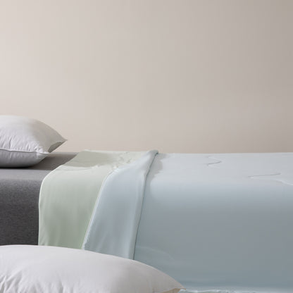 Bed with light blue and gray bedding on a plain background