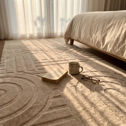 Beige textured rug with a book, mug, and glasses on top, next to a bed with beige bedding.