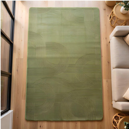 A rectangular sage green area rug with a raised wavy geometric pattern, displayed on a light wood floor in a modern living room setting next to a beige sofa.