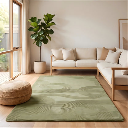 A sage green area rug with a wavy, abstract embossed pattern is styled in a bright, modern living room with a light wood sofa, beige cushions, a potted fiddle-leaf fig, and a woven pouf.