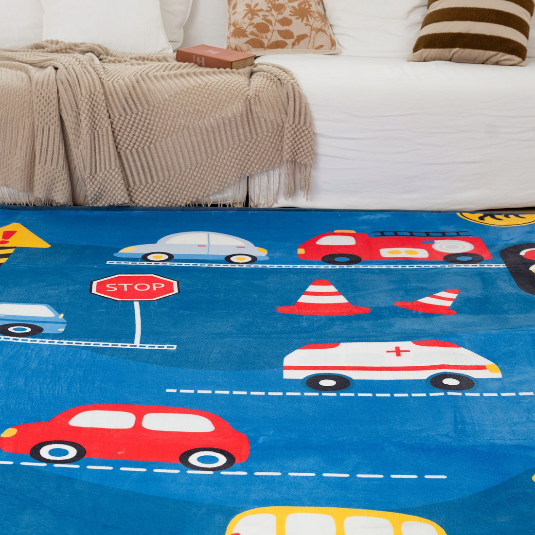 Children's play mat with colorful cars and traffic elements on a blue background, placed in a living room.