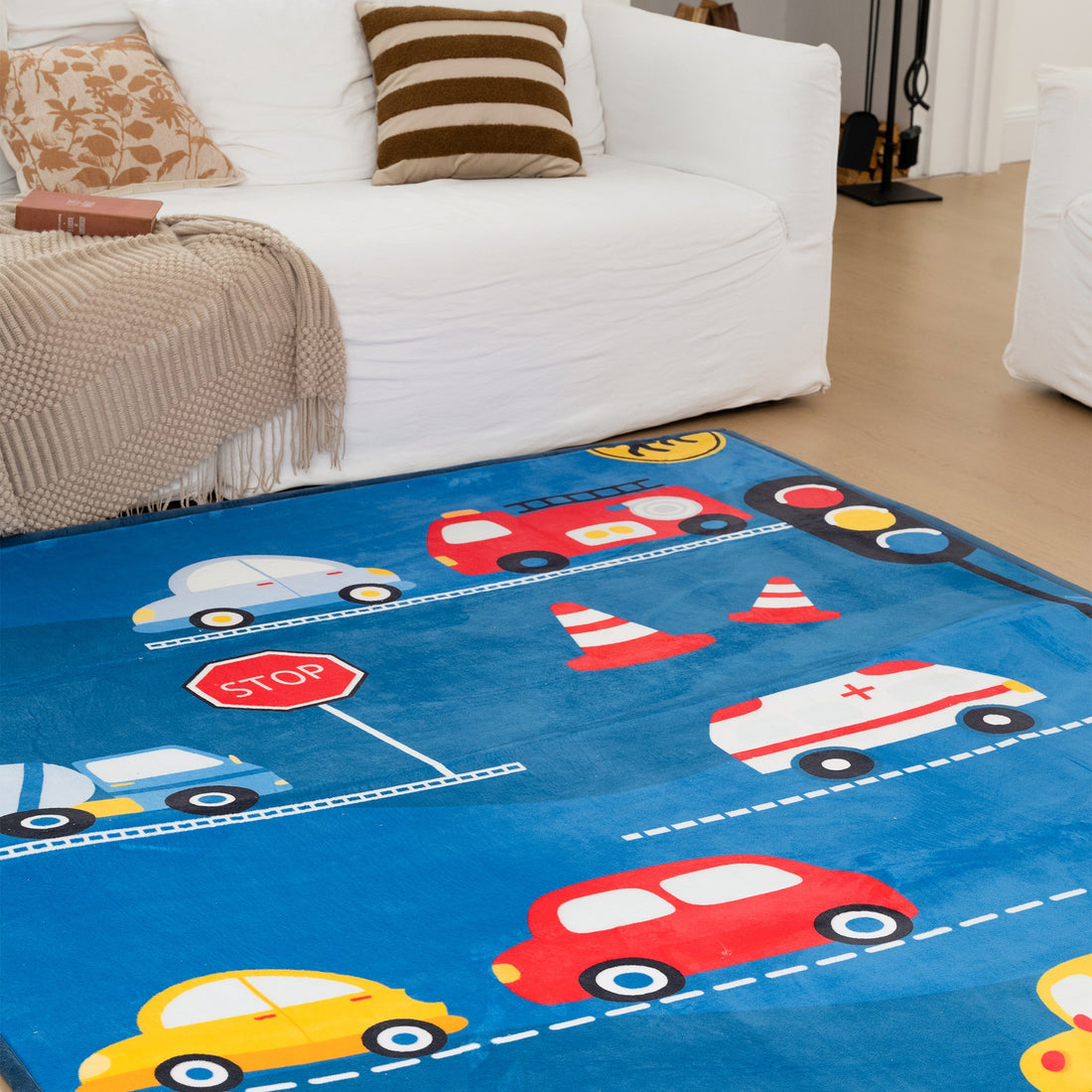 Children's play mat with colorful cars and traffic elements on a blue background, placed in a living room.