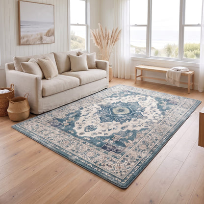 A large rectangular area rug with a traditional medallion pattern in blue, beige, and cream tones, styled on a light wood floor in a bright, modern living room next to a cream sofa.