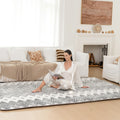 Woman sitting on a patterned mat in a living room with a white couch and fireplace.