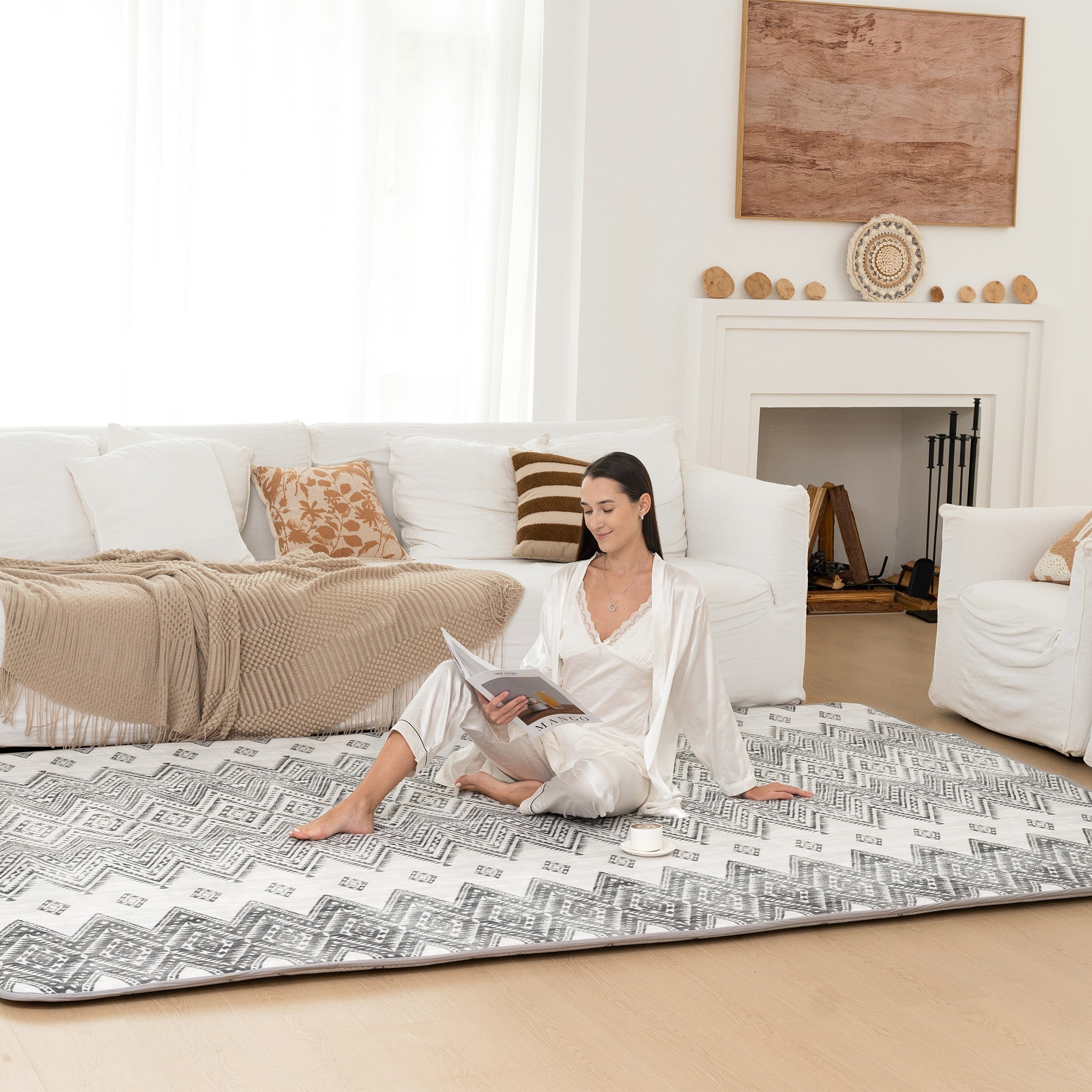 Woman sitting on a patterned mat in a living room with a white couch and fireplace.