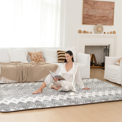 Woman sitting on a patterned mat in a living room with a white couch and fireplace.