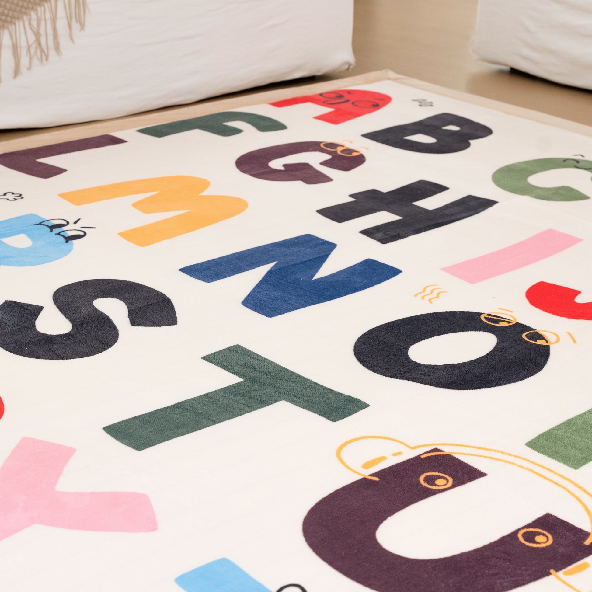 Colorful alphabet rug on a wooden floor with a white couch in the background.