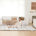 Woman sitting on a large play mat in a living room with a couch and fireplace in the background.
