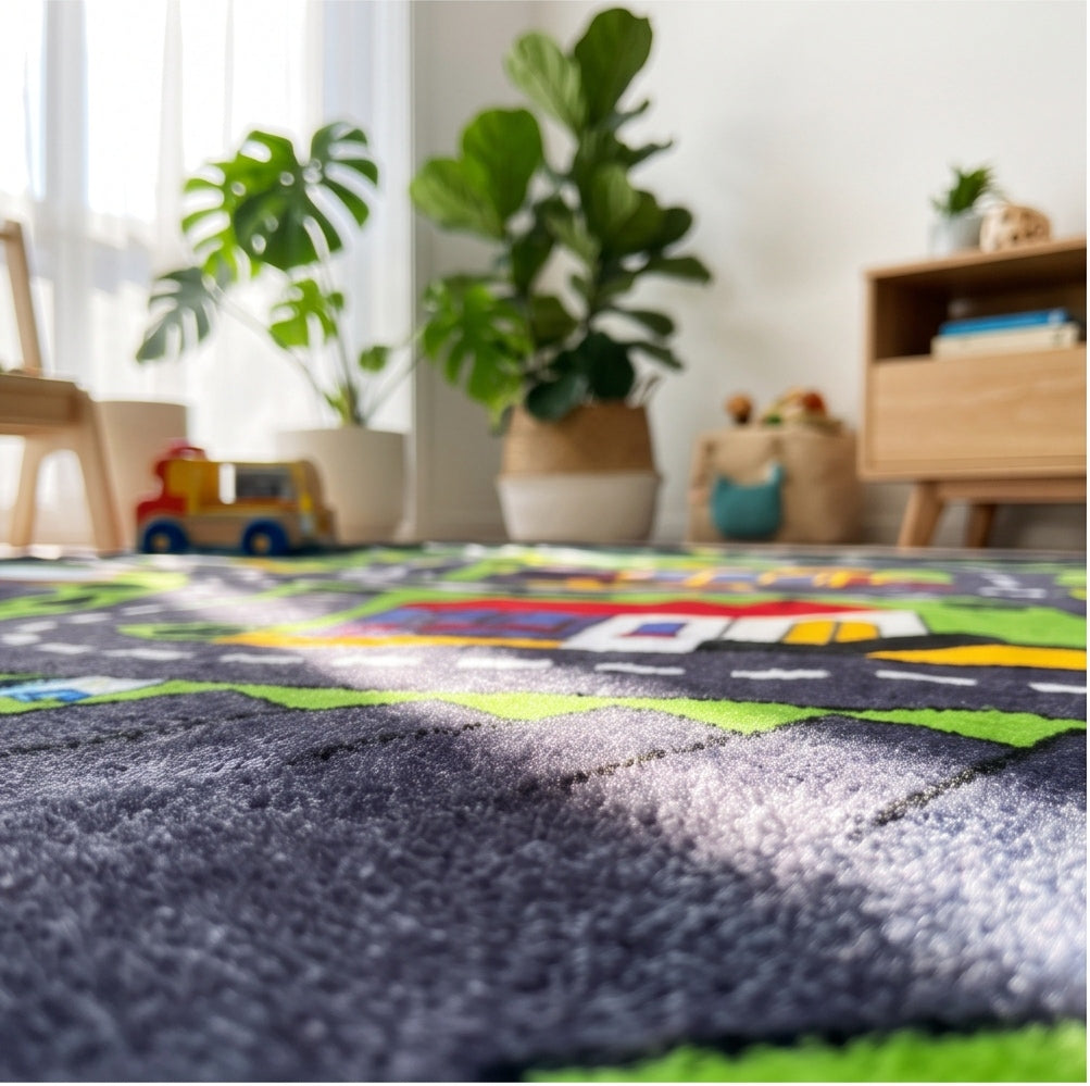 A close-up of a plush dark gray carpet in the foreground, with a colorful children's play rug featuring roads and vehicles visible in the blurred background of a bright, modern room with potted plants and toys.
