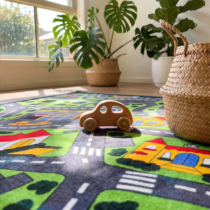 A children's play rug with a colorful road and school town theme, shown in a bright room with plants and wood flooring. The collage includes close-up detail panels of the rug's texture and corner.