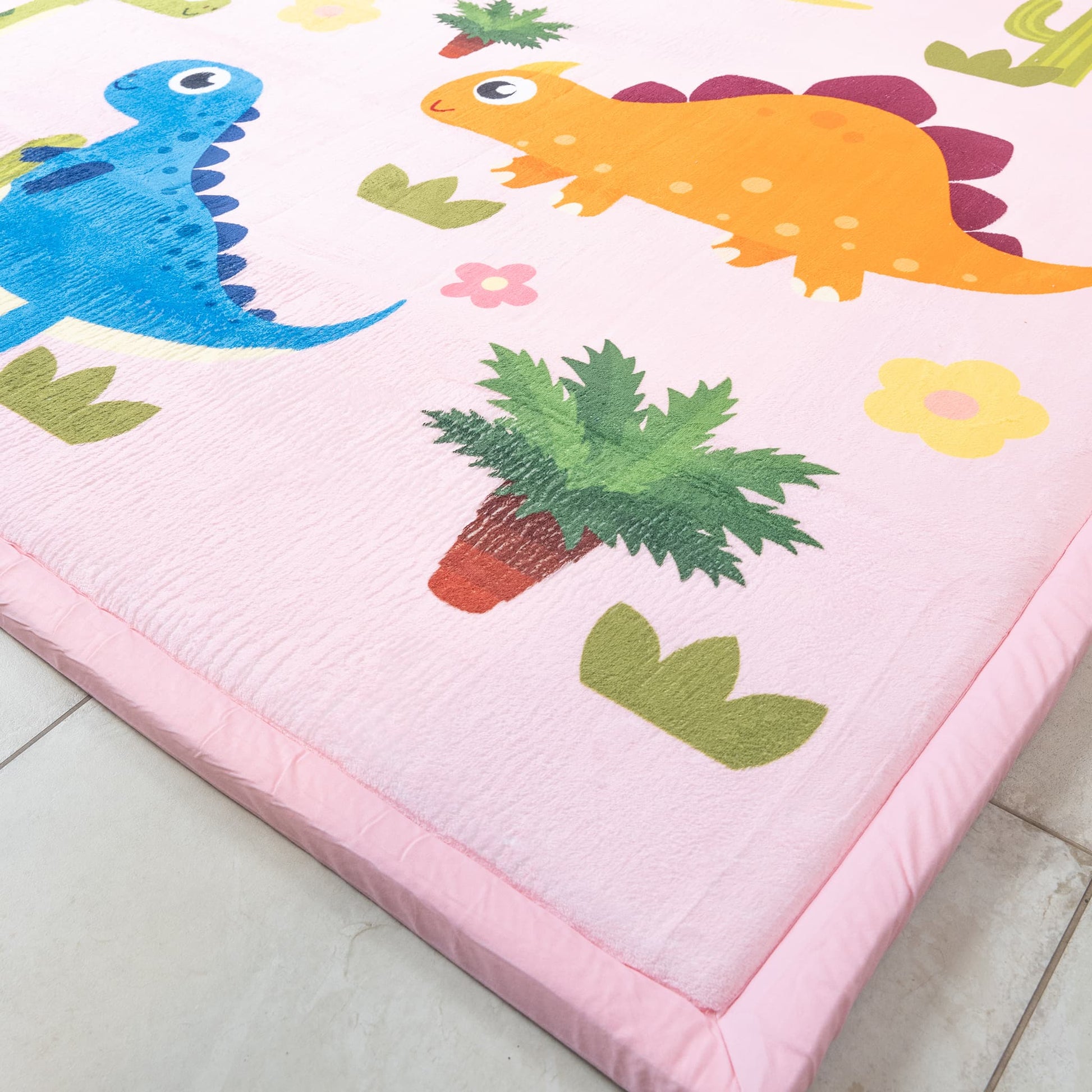 Children's play mat with colorful dinosaur and plant designs on a pink border.