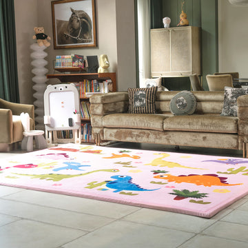 Children's room with a dinosaur rug on the floor, a sofa with cushions, and books on shelves.