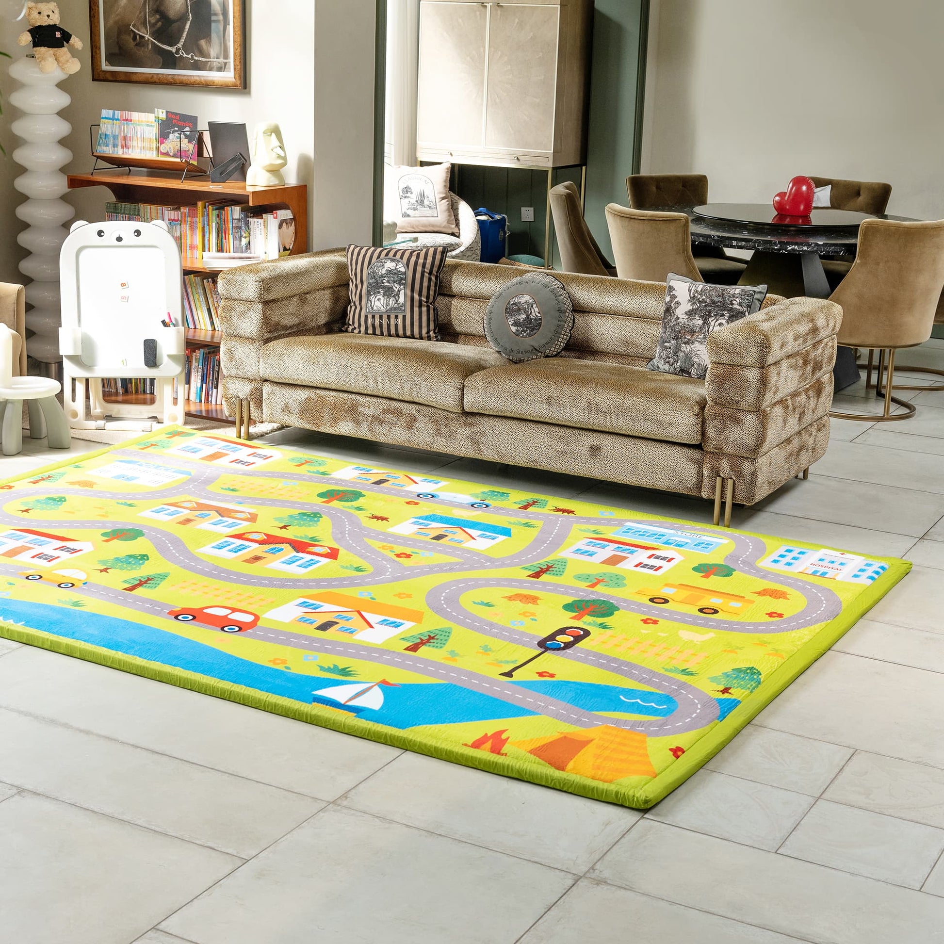 Living room with a colorful children's rug featuring roads and vehicles, a beige sofa with patterned cushions, and a bookshelf.