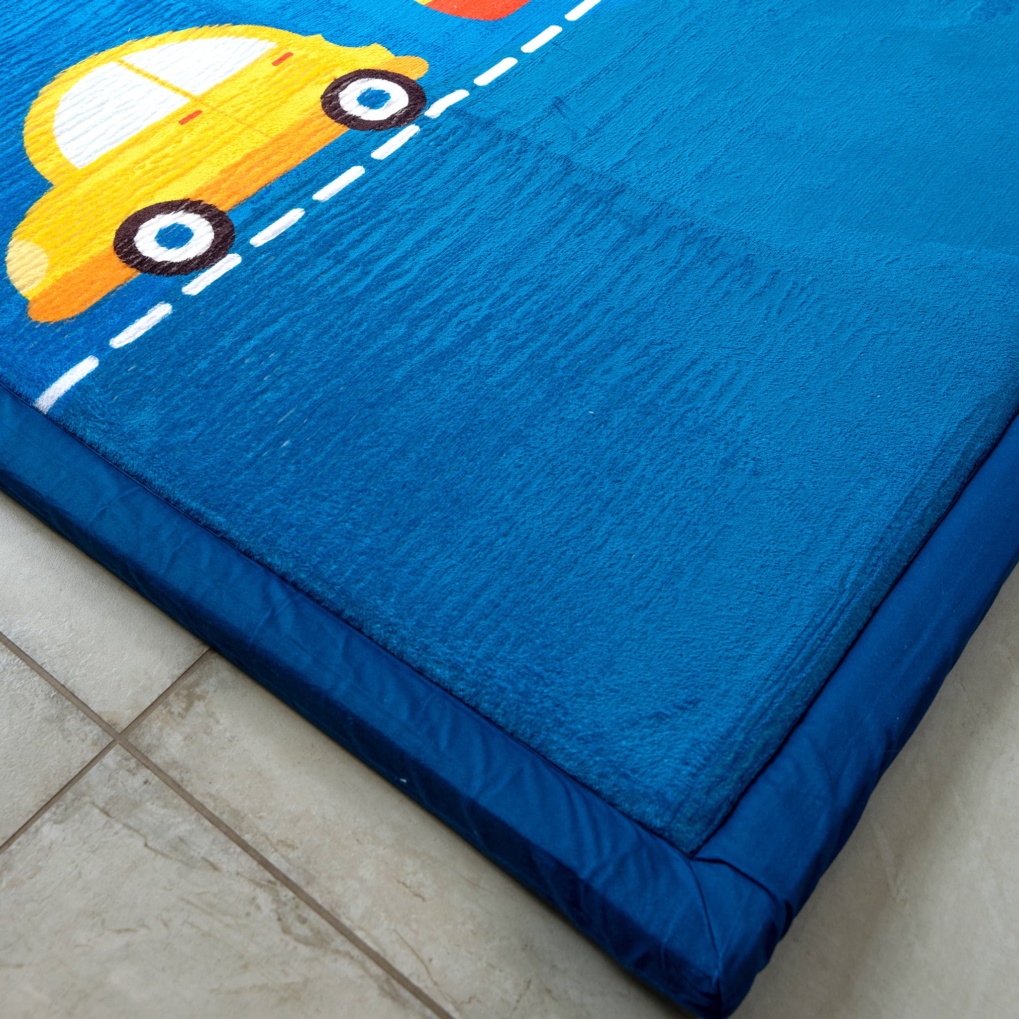 Blue LuxKing cloud mat with yellow car design on a tiled floor