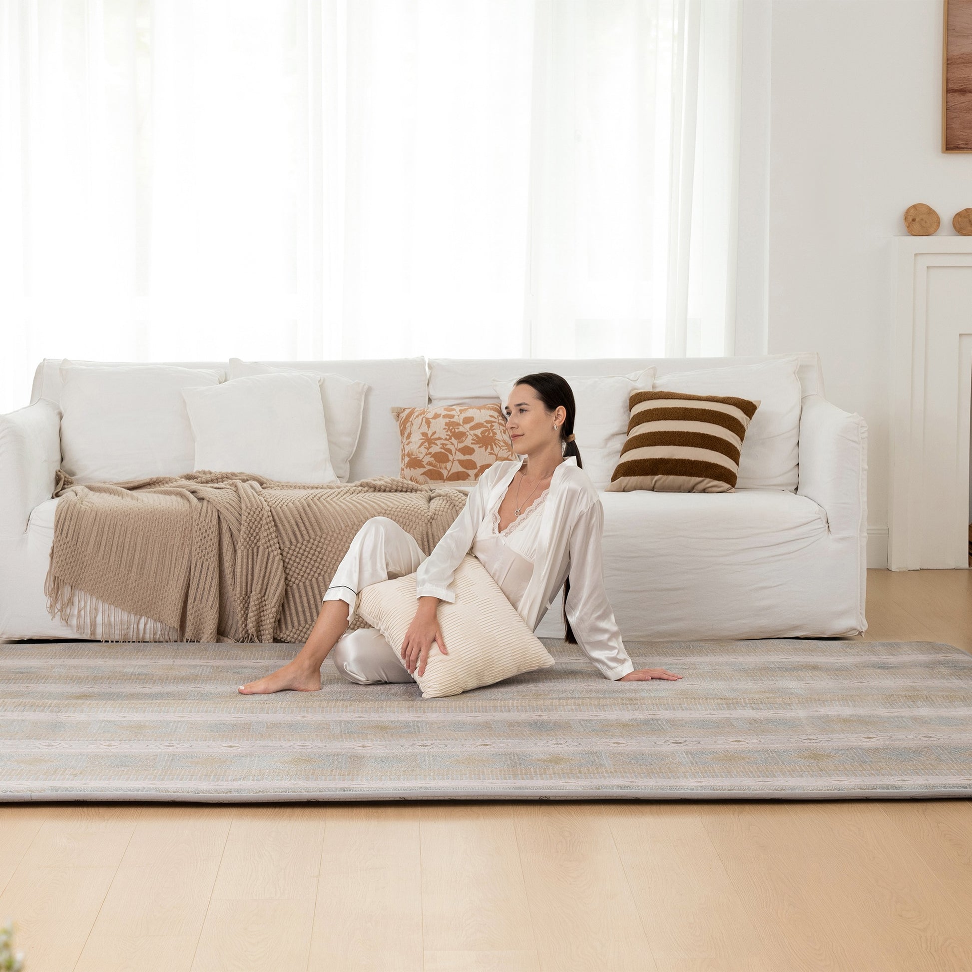 Woman sitting on a white couch with a striped rug in a bright living room.