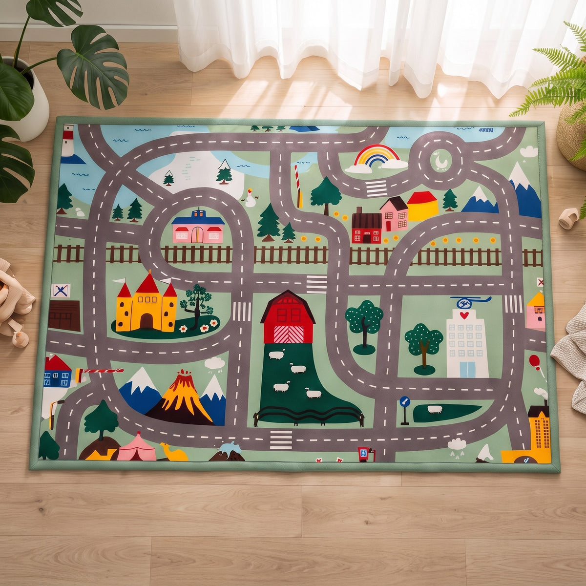 A rectangular children's play rug featuring a whimsical road-map design with houses, trees, mountains, and vehicles, laid out on a light wood floor in a bright room.