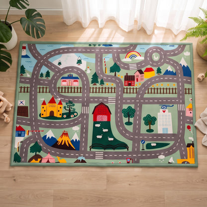 A rectangular children's play rug featuring a whimsical road-map design with houses, trees, mountains, and vehicles, laid out on a light wood floor in a bright room.