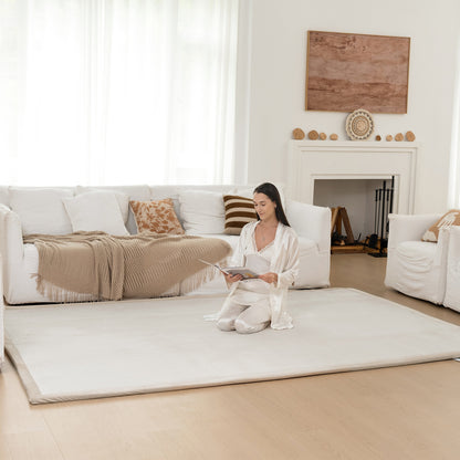 Woman sitting on a white rug in a living room with a fireplace and white sofa.