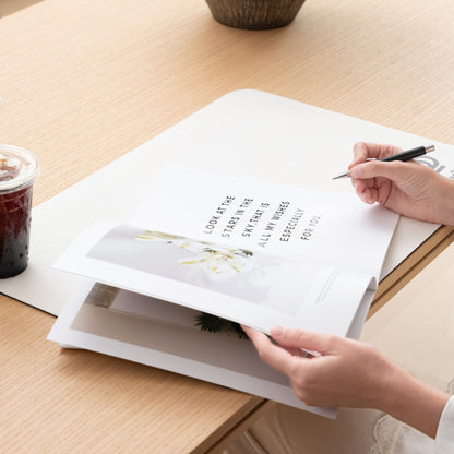 Person holding a pen over a book on a wooden table with a drink beside it