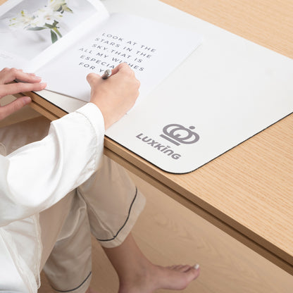 Person writing on a book with a pen, sitting on a wooden floor with a Luxking branded mat.