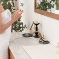 Person applying perfume in a bathroom with decorative items on the sink counter.