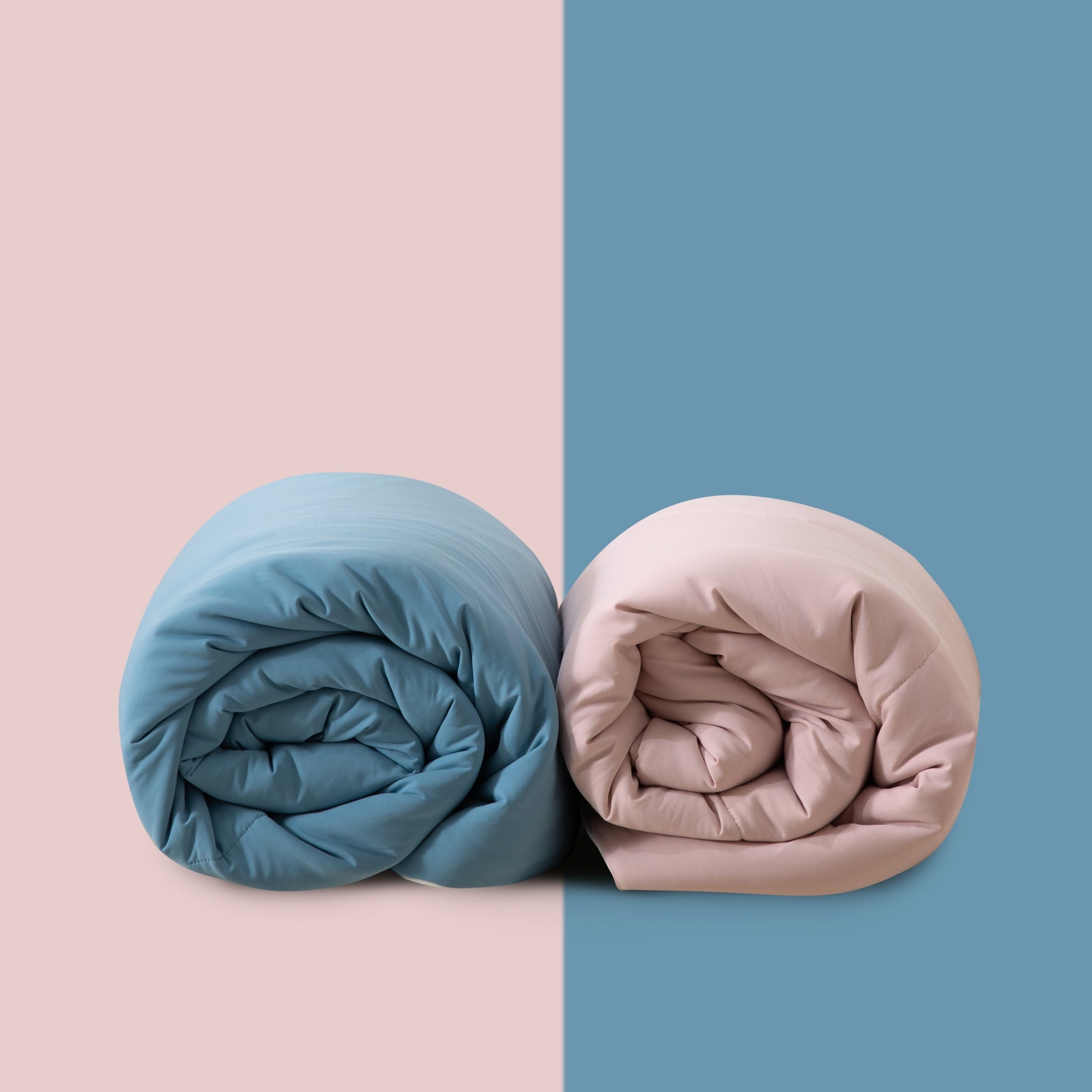 Two rolled-up duvets, one blue and one pink, on a two-tone pink and blue background.