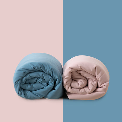 Two rolled-up duvets, one blue and one pink, on a two-tone pink and blue background.