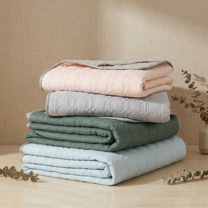 Stack of folded blankets in pastel colors on a wooden surface with a neutral background