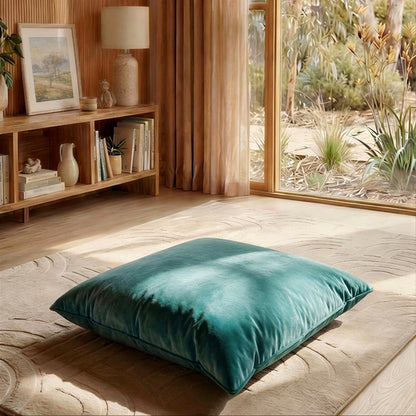 Teal pillow on a wooden floor with a bookshelf and window in the background