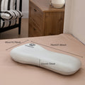 White ergonomic pillow with dimensions labeled on a bed in a bedroom setting