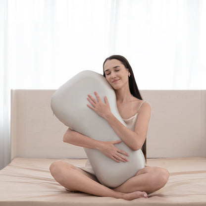 Woman sitting on a bed holding a large U-shaped pillow against a white curtain background